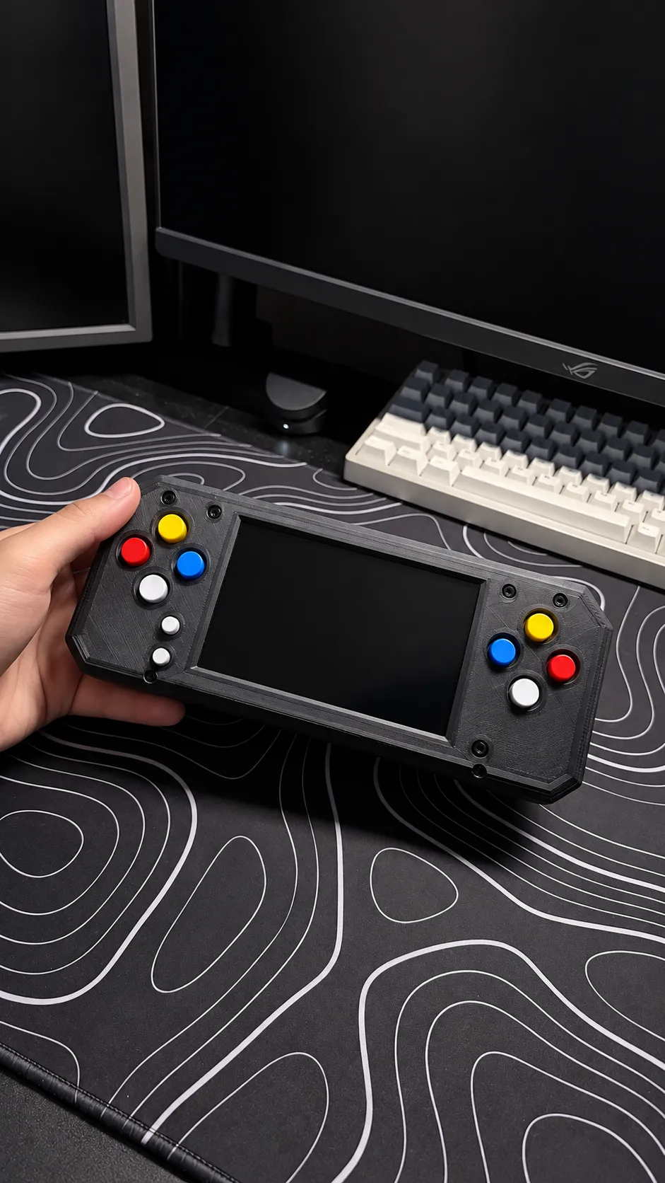 The finished handheld console held in one hand above a desk